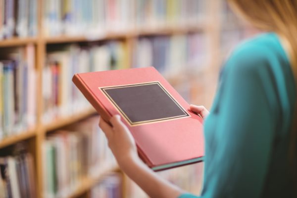 Over shoulder view of student in library holding book at the university